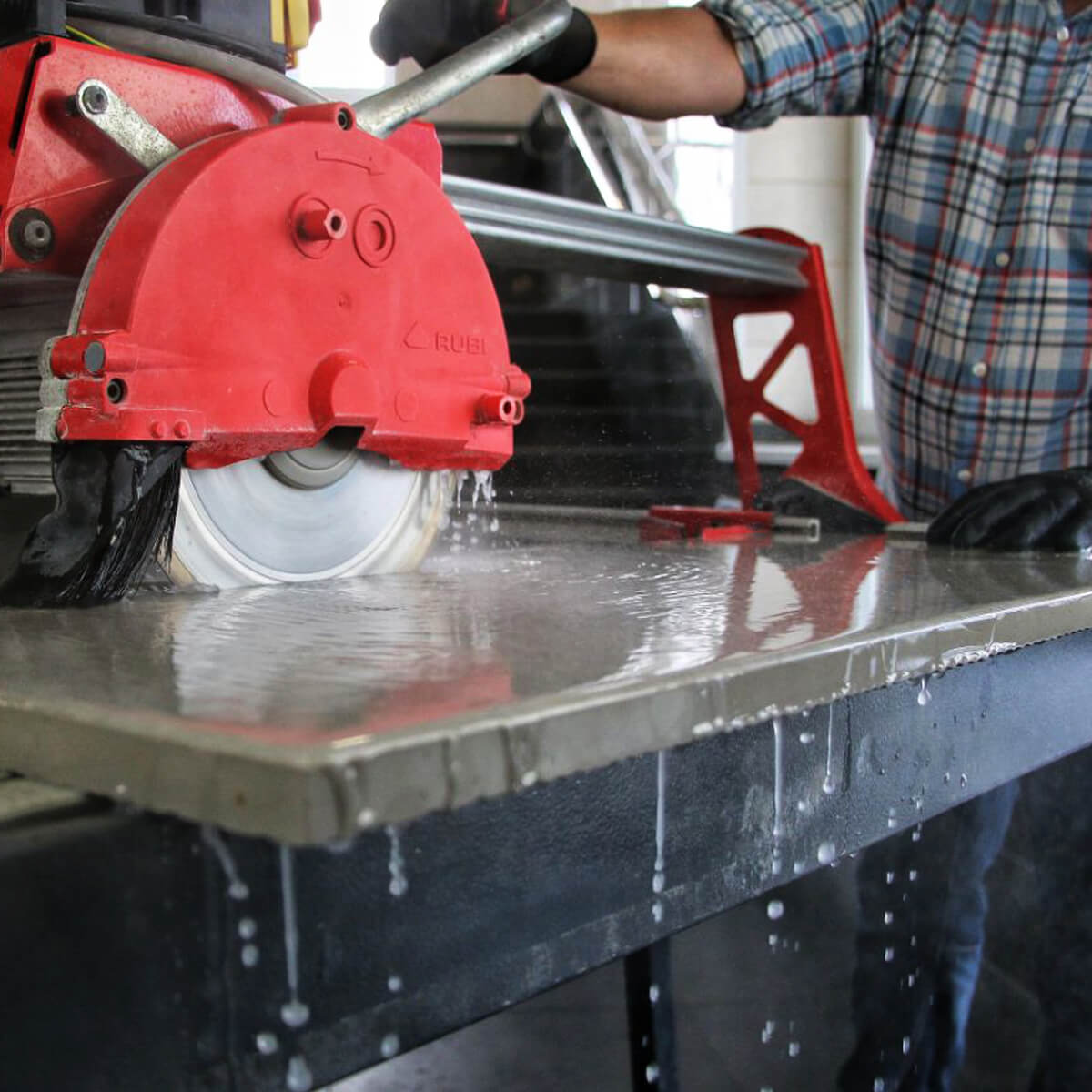 Red circular saw in use on a metal surface with water droplets.